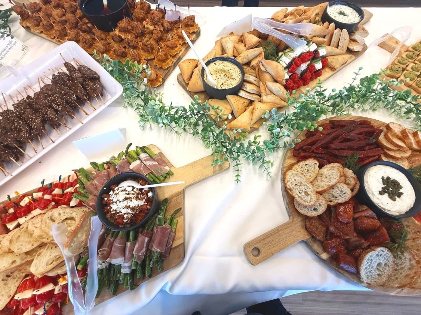 An overhead view of canapé boards: chicken satay skewers, stuffed pita, a charcuterie board, and prosciutto-wrapped asparagus